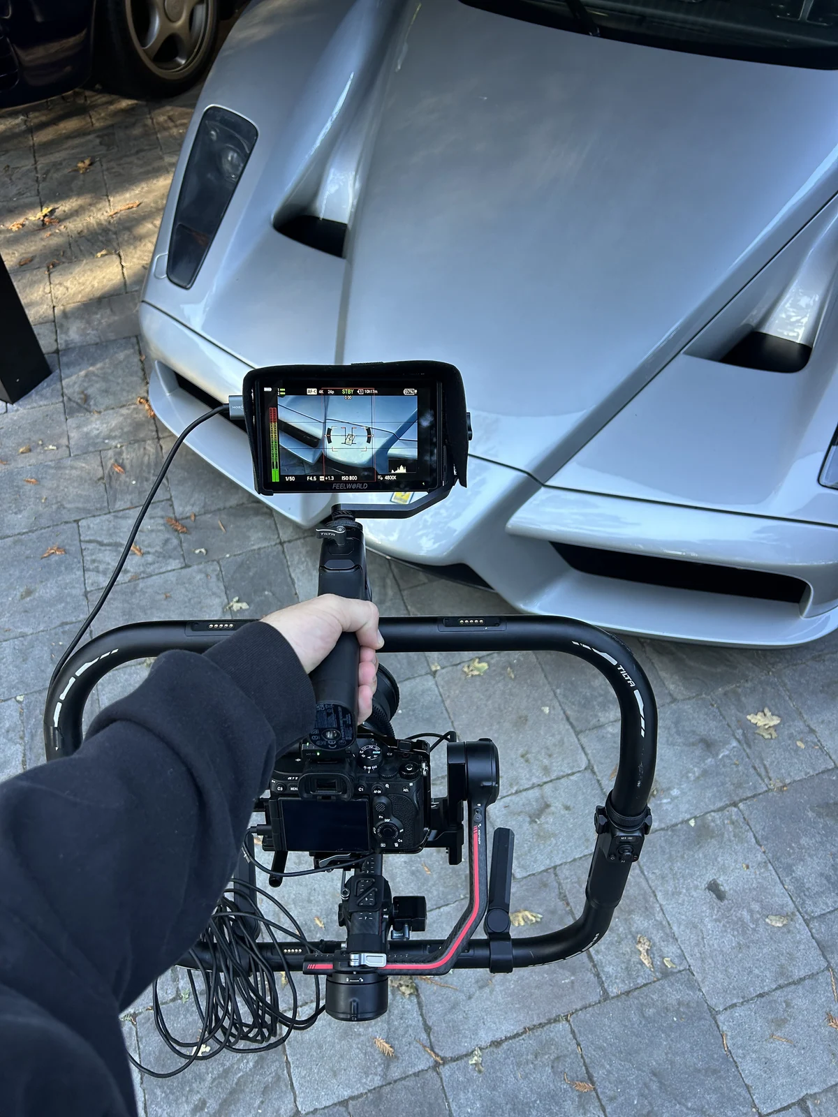 A gimbal and monitor rig in front of a silver Ferrari Enzo