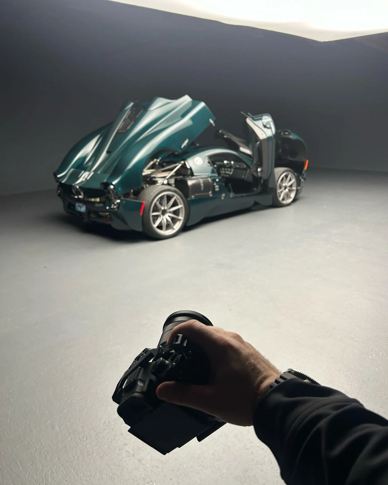 A camera held out towards a Pagani Utopia with its doors open in a grey studio