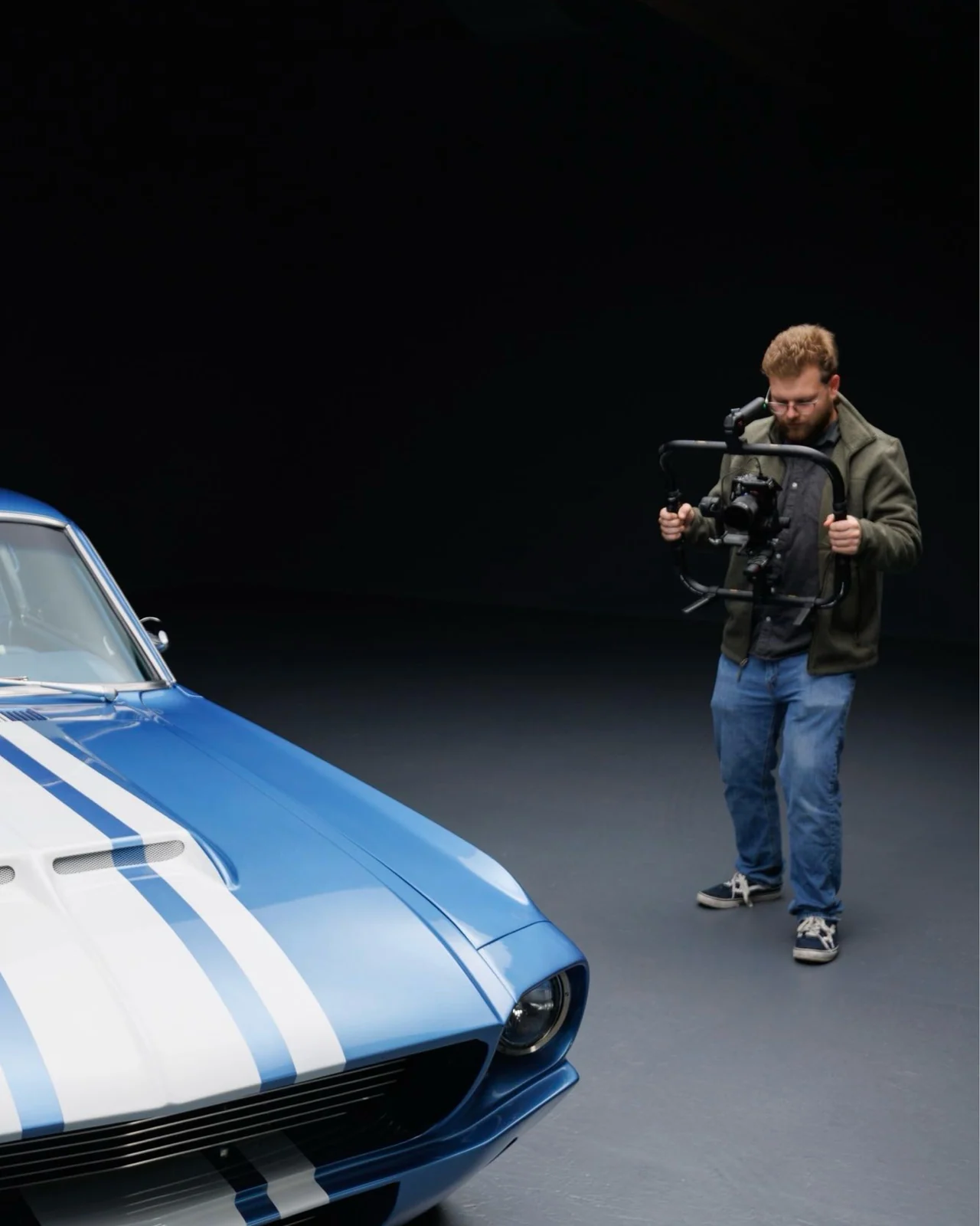 Max filming with a gimbal beside a blue and white Mustang in the studio