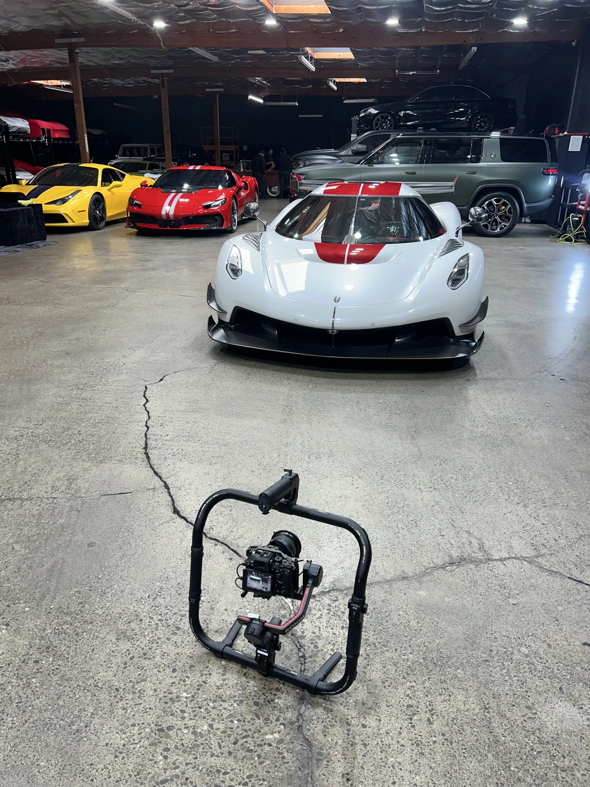 A camera gimbal on the floor in front of a white Koenigsegg Jesko