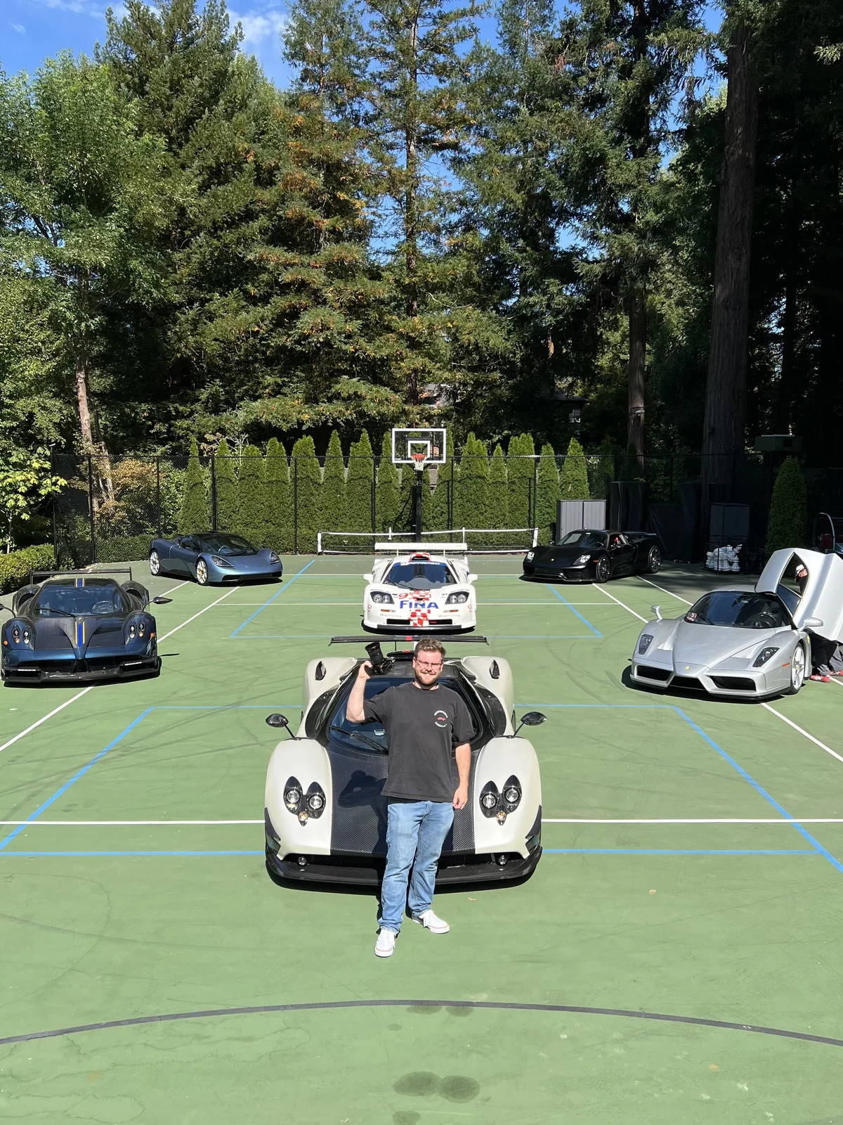 Max standing with a Pagani Zonda among a private collection of hypercars on a tennis court